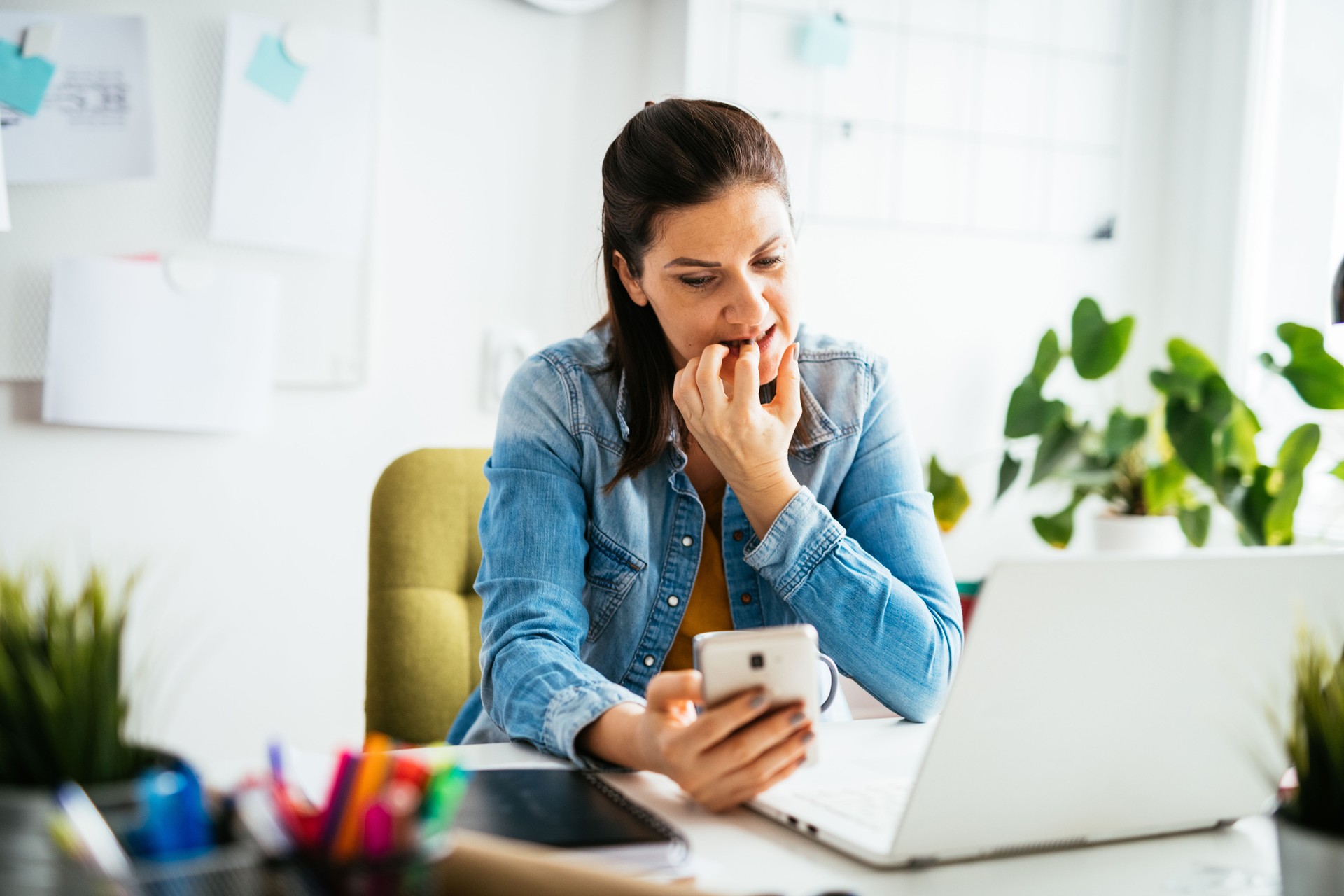 Anxious woman working in office and using smart phone, woman biting her fingers and nails