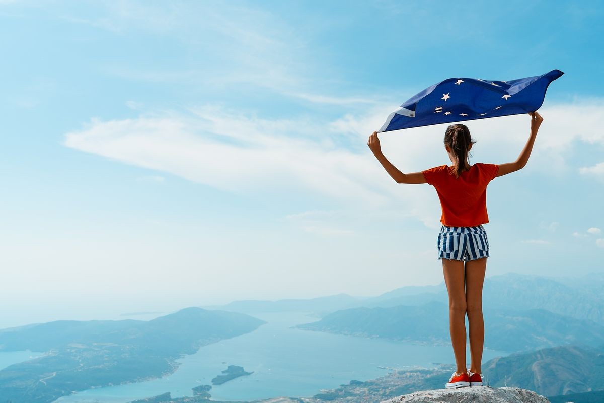 Child girl teenager young person is waving European Union flag on top of mountain at sky background